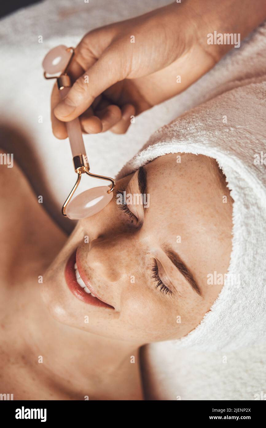 Der Patient erhält im Spa-Salon eine Anti-Aging-Gesichtsmassage mit dem Gesichtsmassager Jade Roller. Schönheitshaut. Beauty Face. Schönheitsbehandlung. Hautpflege. Stockfoto