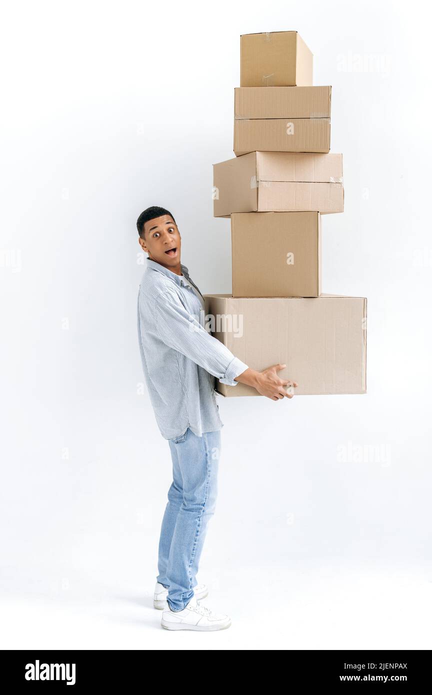 Aufgeregt gemischter Renner in lässiger, stilvoller Kleidung, Lieferer, der auf isoliertem weißem Hintergrund steht, viele Kartons hält, Pakete liefert, erstaunt auf die Kamera schaut, Lieferung Stockfoto