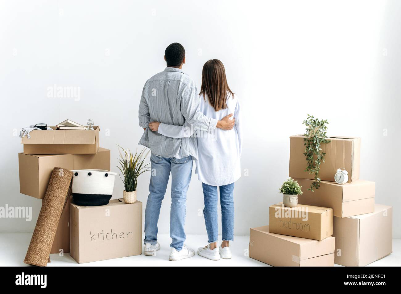 Neue Wohnungen, Umzug. Glückliches junges multirassisches Paar, stehen mit dem Rücken zur Kamera zwischen Kisten mit Sachen in ihrem neuen Zuhause oder Mietwohnung, und planen ihr zukünftiges Haus-Design Stockfoto