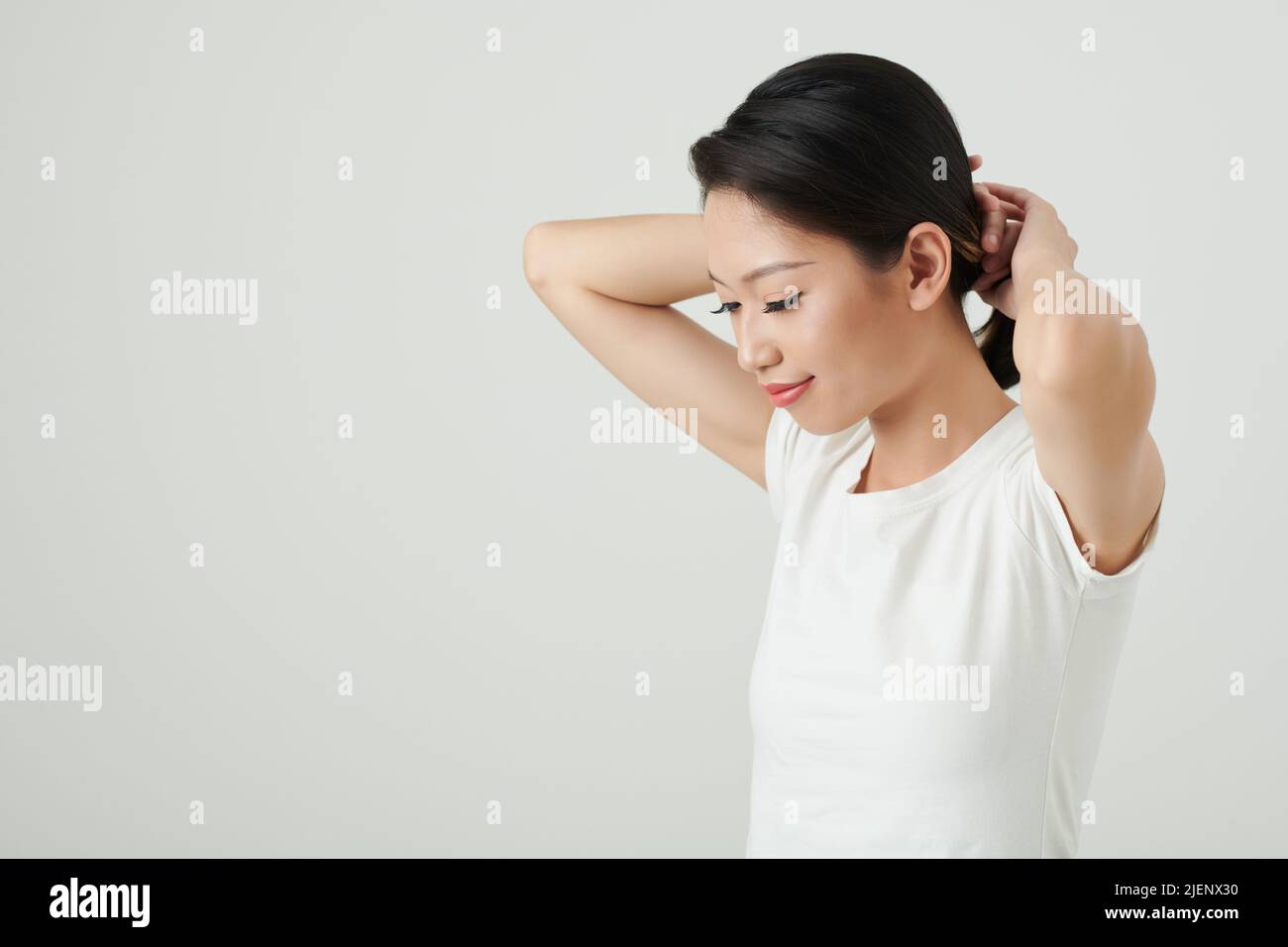Sudio-Porträt einer lächelnden jungen asiatischen Frau in weißem T-Shirt, das Pferdeschwanz macht Stockfoto