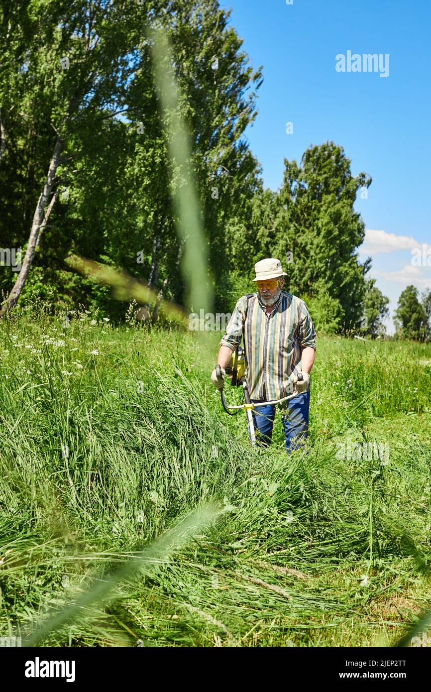 Ein Mann mäht das Gras auf dem Feld mit einem Trimmer. Gartenpflege-Konzept. Vertikales Foto. Stockfoto