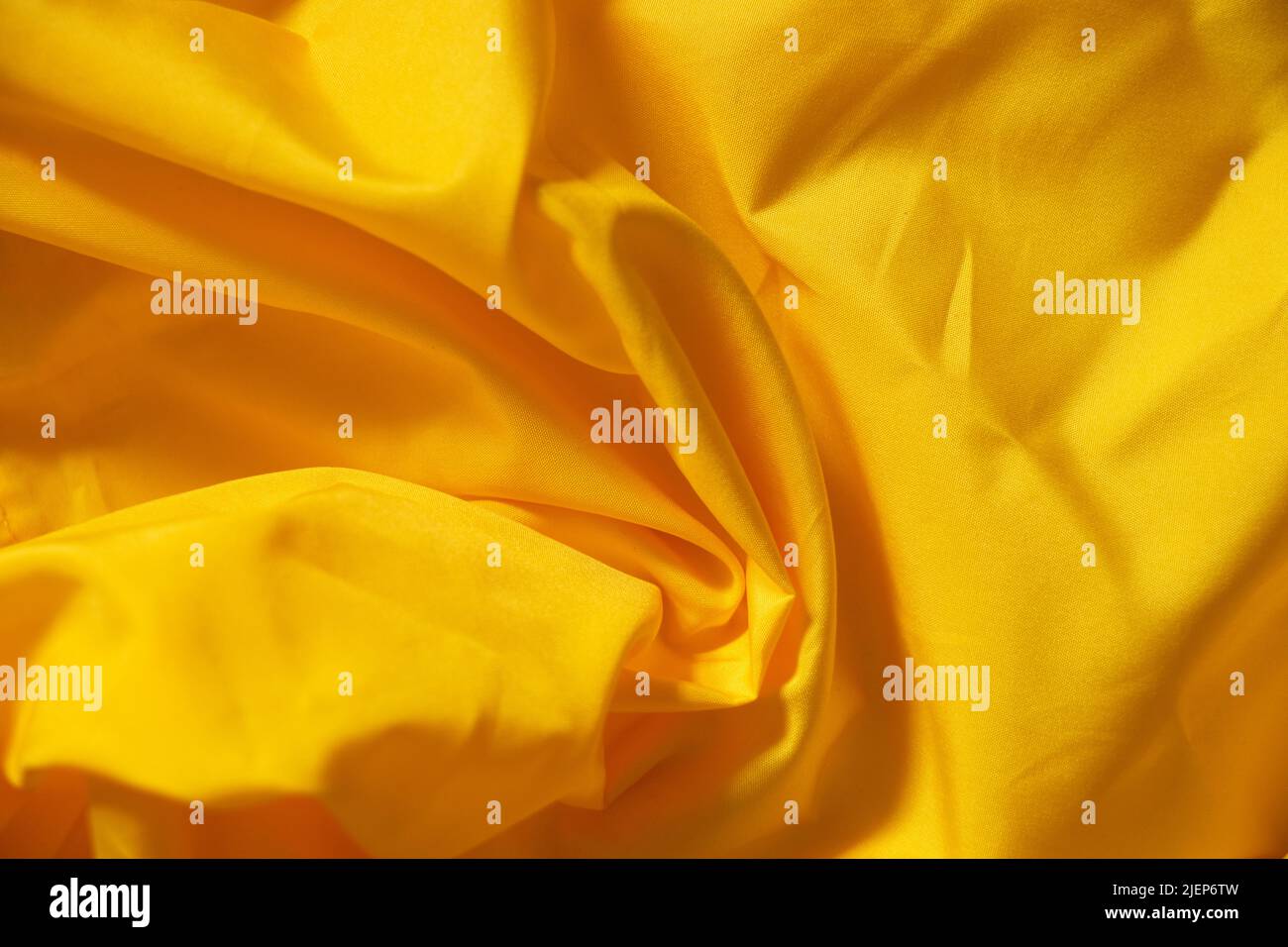 Seidengelber, zerknitterter Stoff als Hintergrund in Nahaufnahme, gelber Hintergrund Stockfoto
