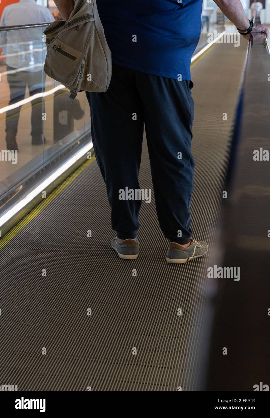 Ein Mann mit Rucksack, der auf einem beweglichen Gang am Flughafen stand. Passagiere, die zum Terminal Gate fahren, reisen mit speziellen Assistenzkonzepten Stockfoto