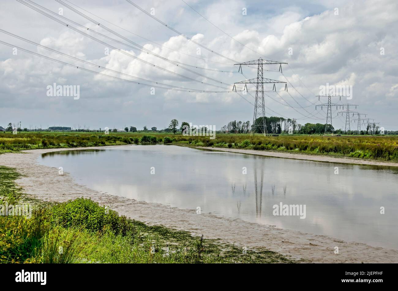 Strommasten und Stromleitungen spiegeln sich an einem Sommertag in der Region Noordwaard im Nationalpark Biesbosch in einem Gewässer mit schlammigen Bänken wider Stockfoto