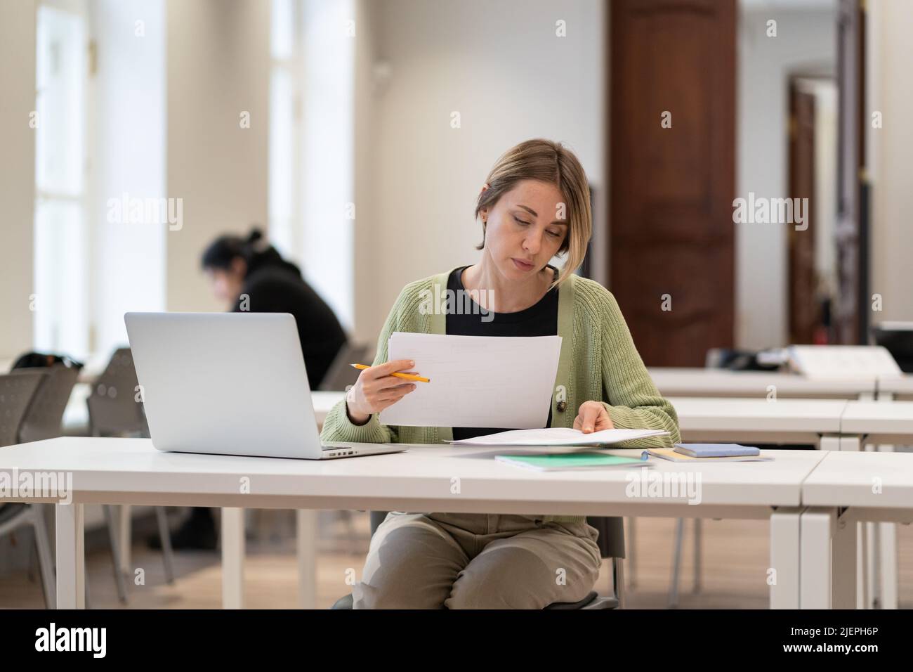 Fleißige reife Studentin, die Architekturzeichnungen liest, während sie in der öffentlichen Bibliothek studiert Stockfoto