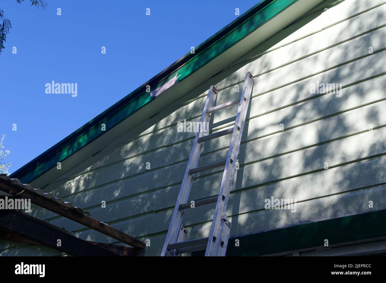 Eine Leiter lehnt sich an ein Wetterbretthaus, vielleicht ist sie da, damit jemand das kaputte Dach an der Seite befestigen kann. Stockfoto