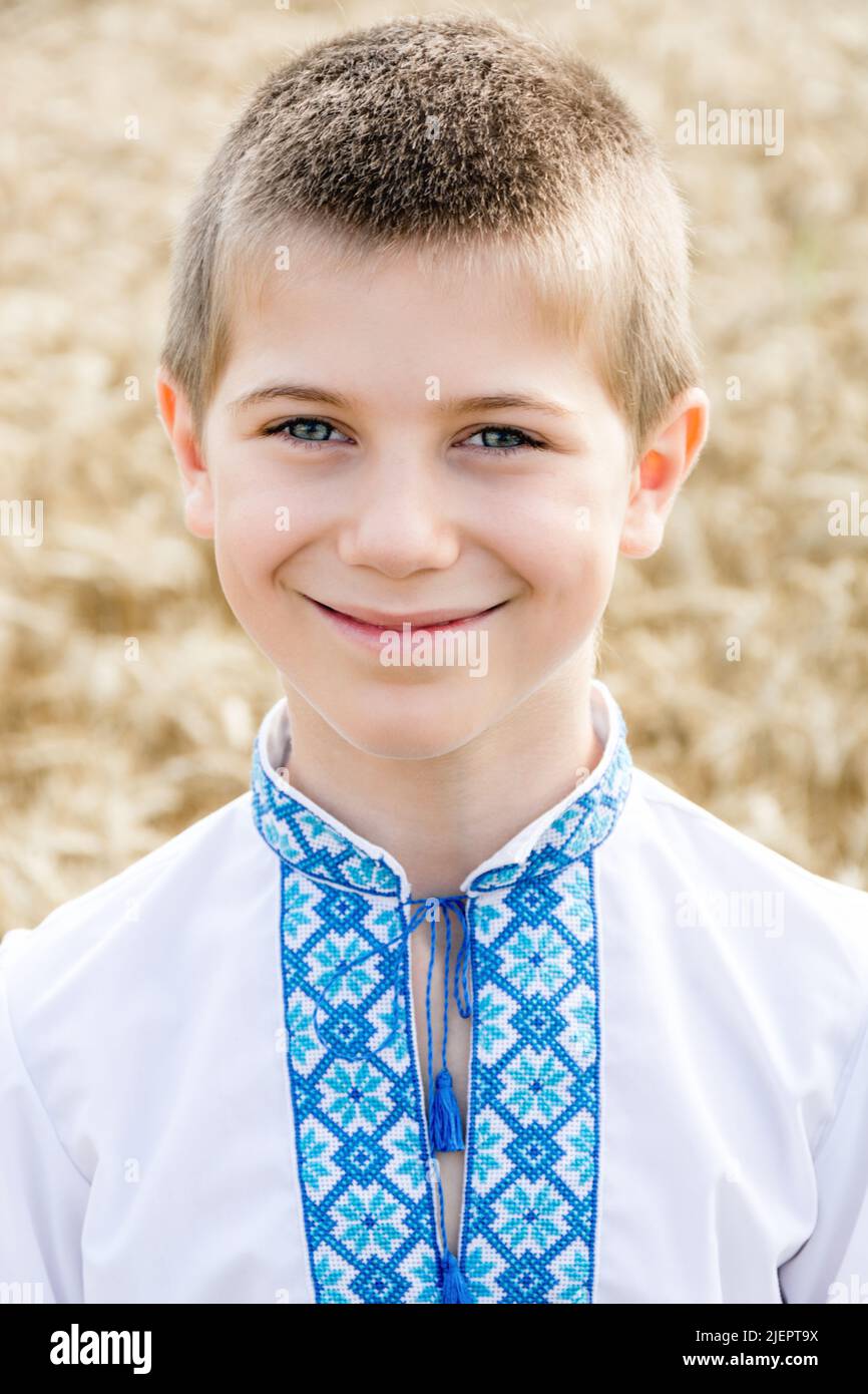 Porträt des Kindes in traditionellen bestickten ukrainischen Hemd auf dem Hintergrund des Weizenfeldes an sonnigen Tag. Blaue Stickerei. Junge lächelt aufrichtig. Unabhängigkeitstag, Verfassung der Ukraine. Vertikal Stockfoto