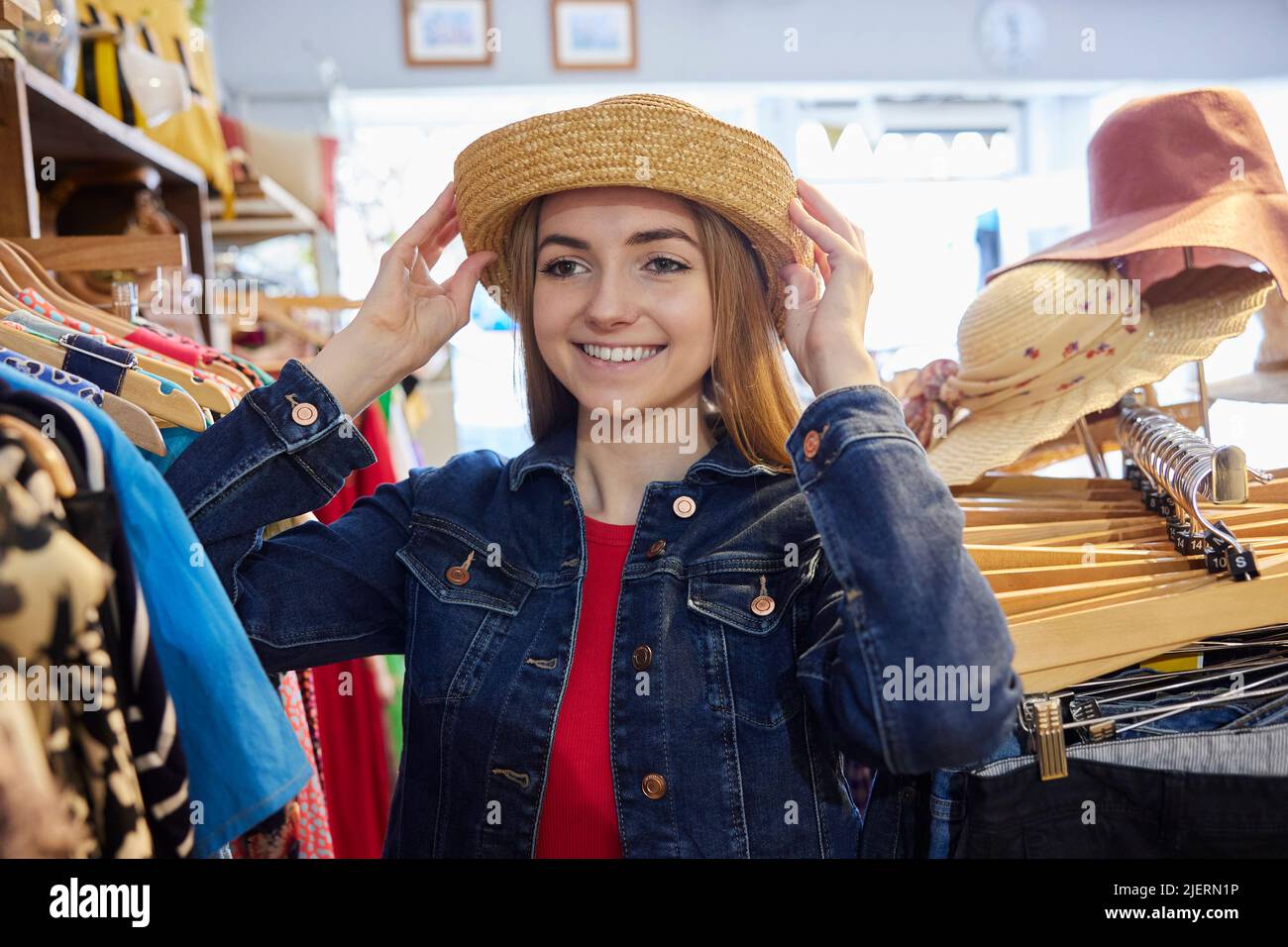 Junge Frau, Die Gebrauchte Nachhaltige Kleidung Aus Dem Second Hand Charity Shop Kauft, Versucht Auf Hut Stockfoto