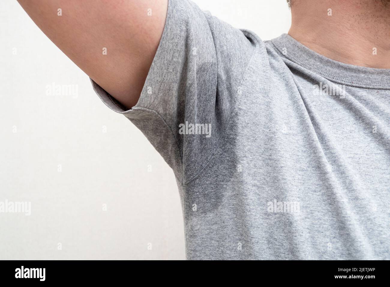 Verschwitzte Achselhöhlen, nasser Achselfleck auf grauem T-Shirt Stockfoto