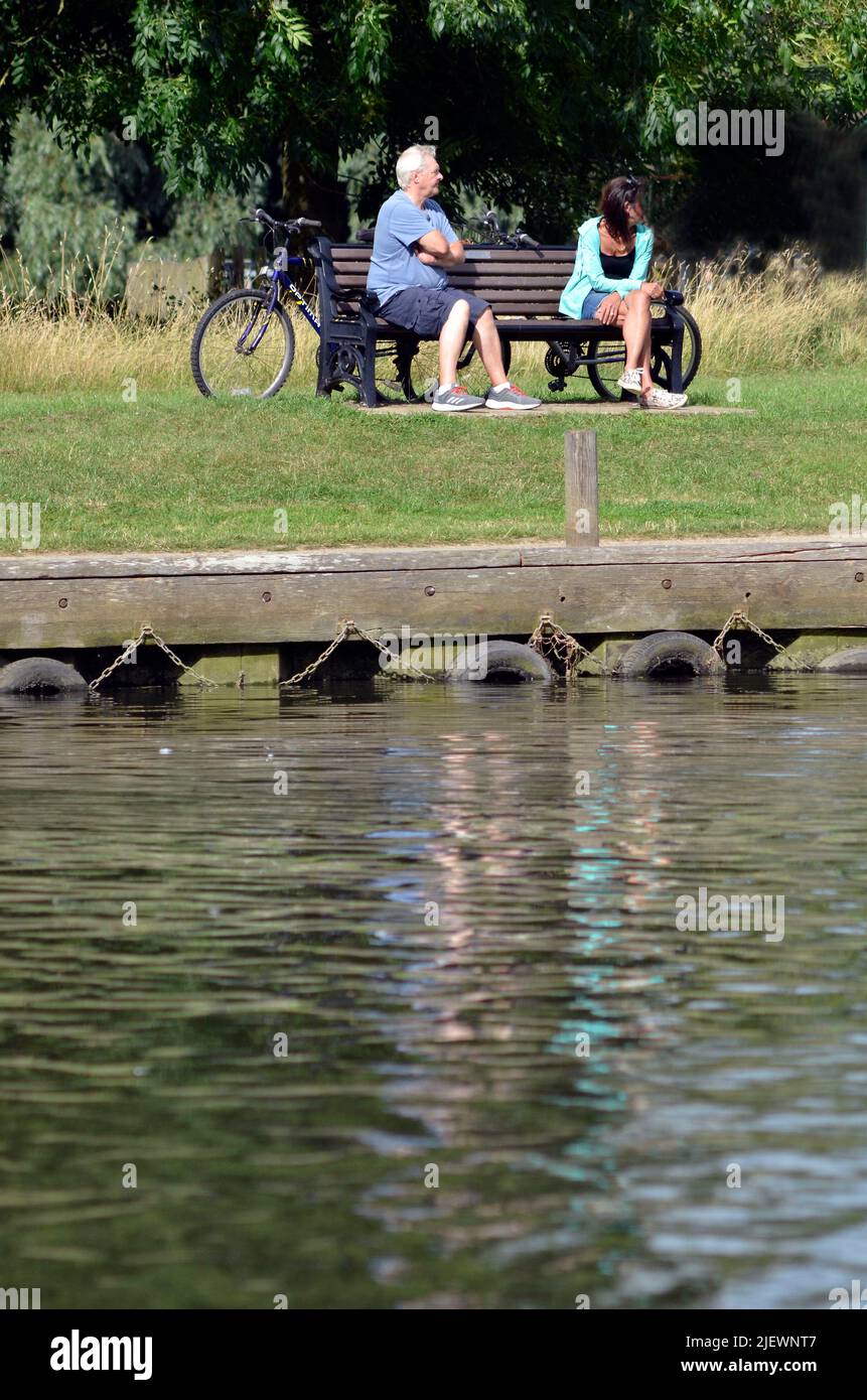 Älterer Mann und jüngere Frau sitzen auf einer Bank am Fluss beccles suffolk england Stockfoto