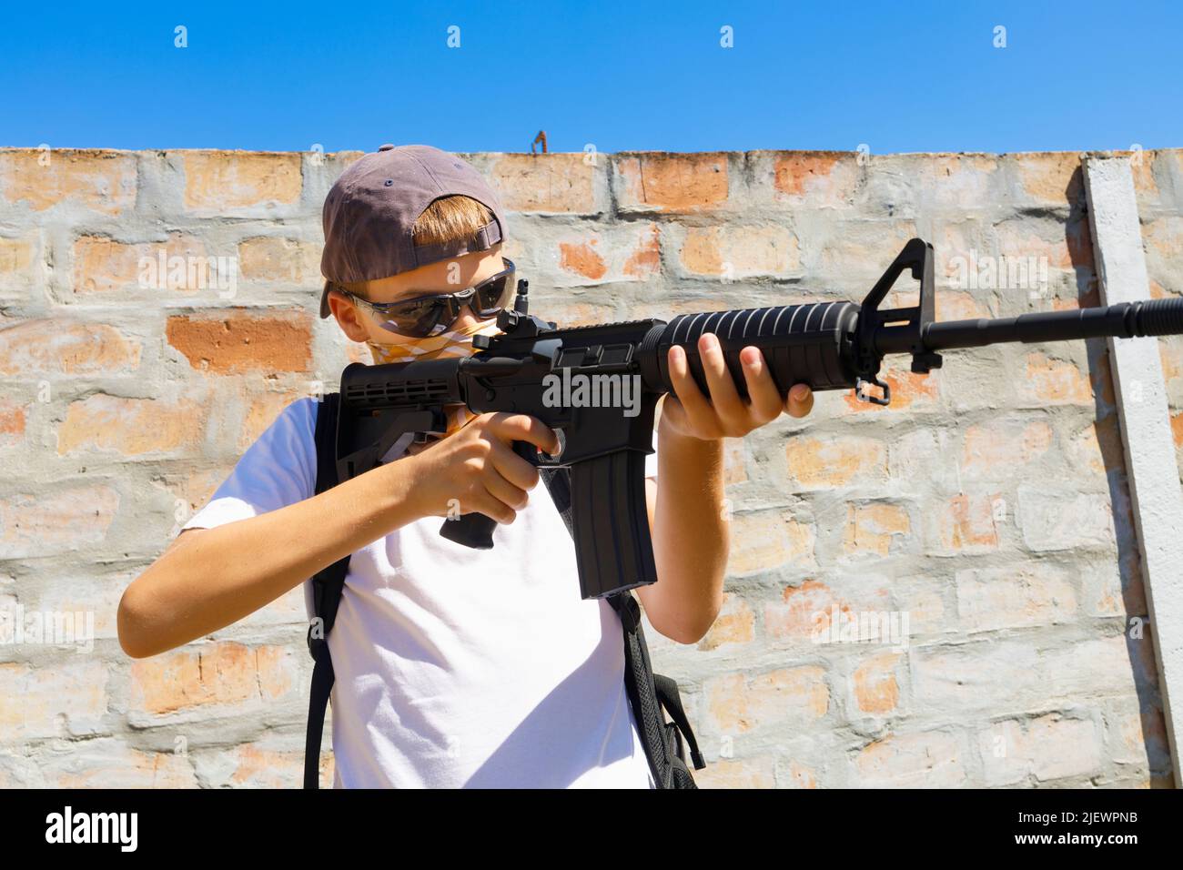 Ein Kind, das sein automatisches M4A1 Gewehr anvisieren will. Konzept für Schulaufnahmen. Stockfoto