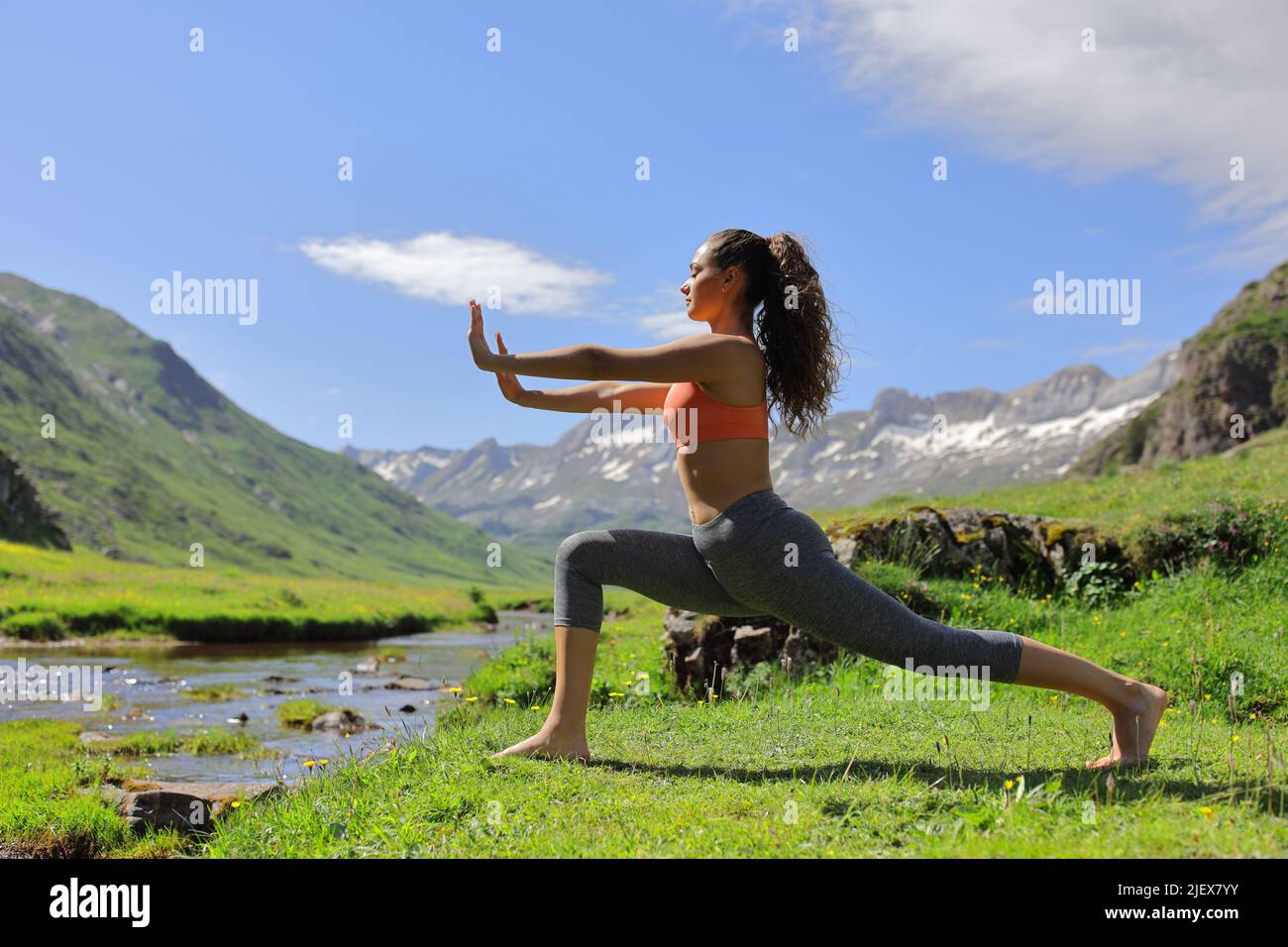 Seitenansicht Porträt einer Frau, die auf dem grünen hohen Berg neben einem Fluss Tai Chi praktiziert Stockfoto