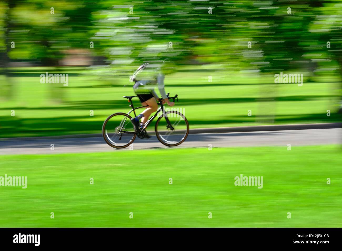 Person, die im Sommer Fahrrad oder Fahrrad im grünen Park fährt, bewegt sich schnell verschwommene Geschwindigkeit verschwommene Bewegung Stockfoto