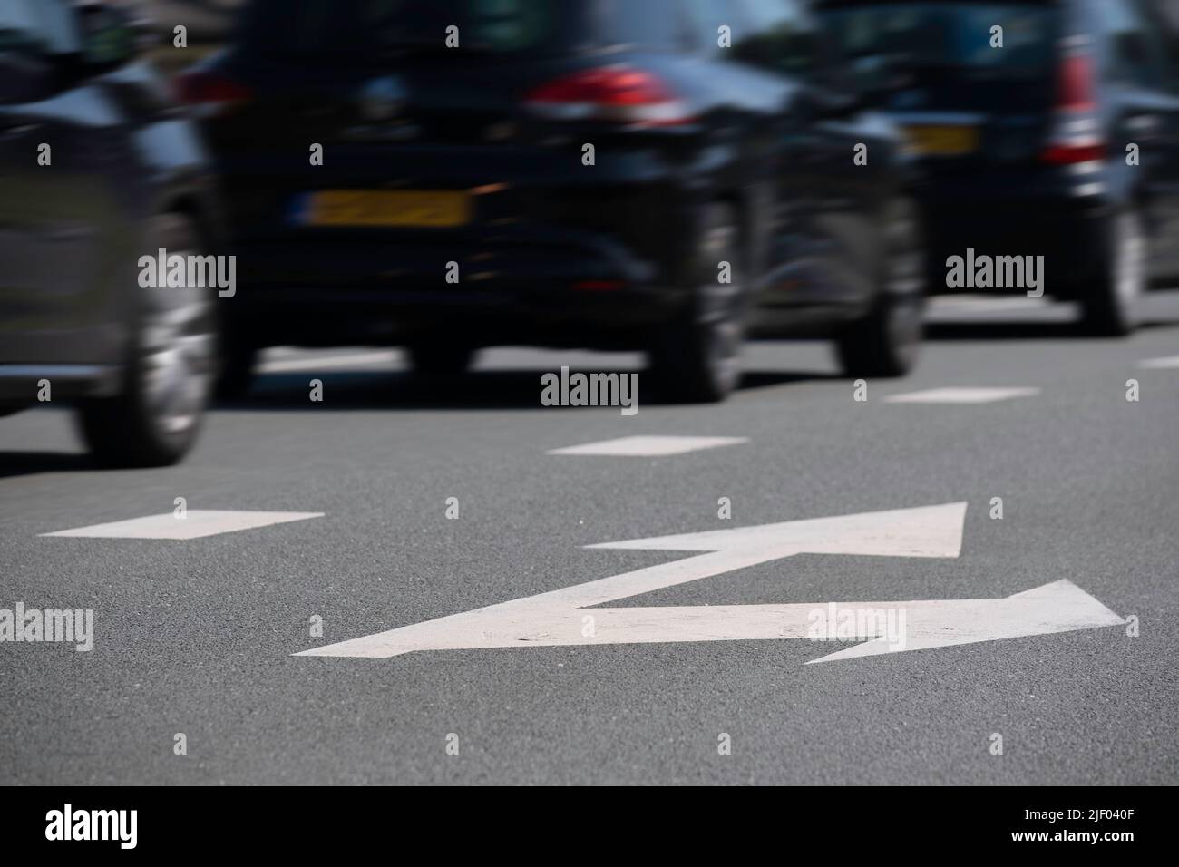 Dunkle Autos fahren nacheinander auf einer asphaltierten Straße auf einer Spur. Die rechte Spur mit den Pfeilen geradeaus und rechts ist leer. Konzentrieren Sie sich auf die Stockfoto