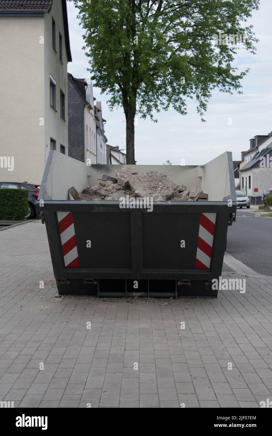 Grauer Behälter oder Müllcontainer mit Bauschutt oder Bauabfall. Container wird auf dem Bürgersteig in einem Wohngebiet platziert. Stockfoto