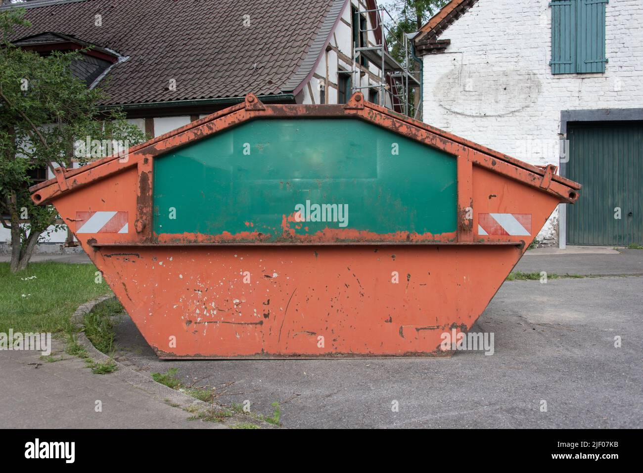Seitenansicht eines orange-grünen Behälters oder Müllers. Der Container steht vor einem historischen Gebäude, das gerade umgebaut wird. Stockfoto