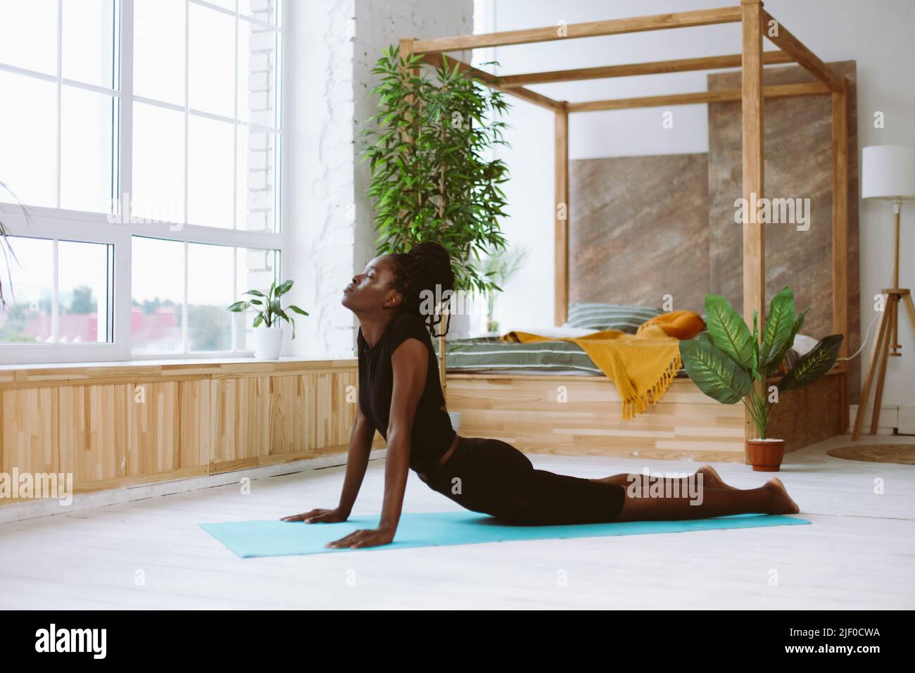 Achtsame dunkle Haut afroamerikanische Frau mit geschlossenen Augen machen Yoga-Übungen im Haus. Entspannen und Stretching in Kobra Pose Stockfoto