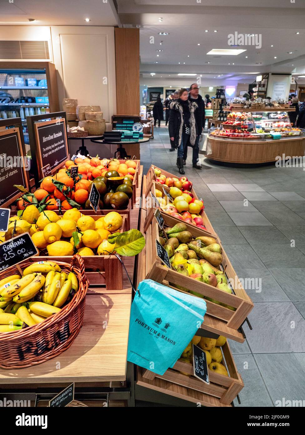 Fortnum & Mason Food Hall mit offener Ausstellung von Obst und Gemüse zum Verkauf mit Fortnums Marken-Recycling-Papiertüten, die für den bequemen Einkauf platziert werden. Ananas Bananen und Äpfel in Korbkörben. Fortnum & Mason Food Hall Department, Piccadilly St. James's, London W1A 1ER Stockfoto