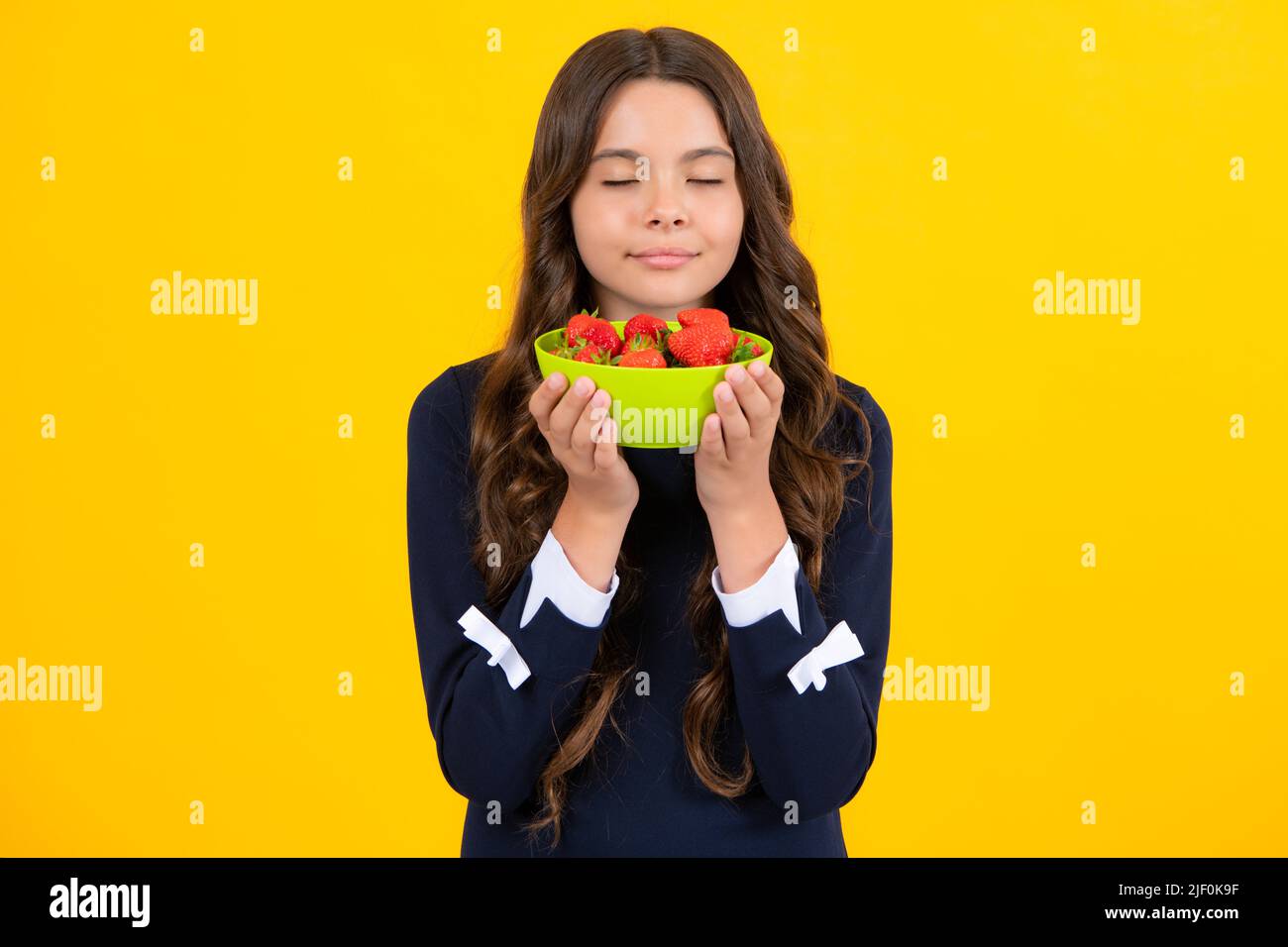 Kind, das Erdbeeren isst. Glücklich lächelndes jugendliches Kind halten Erdbeerschale auf gelbem Hintergrund. Gesunde natürliche Bio-Vitaminnahrung für Kinder Stockfoto