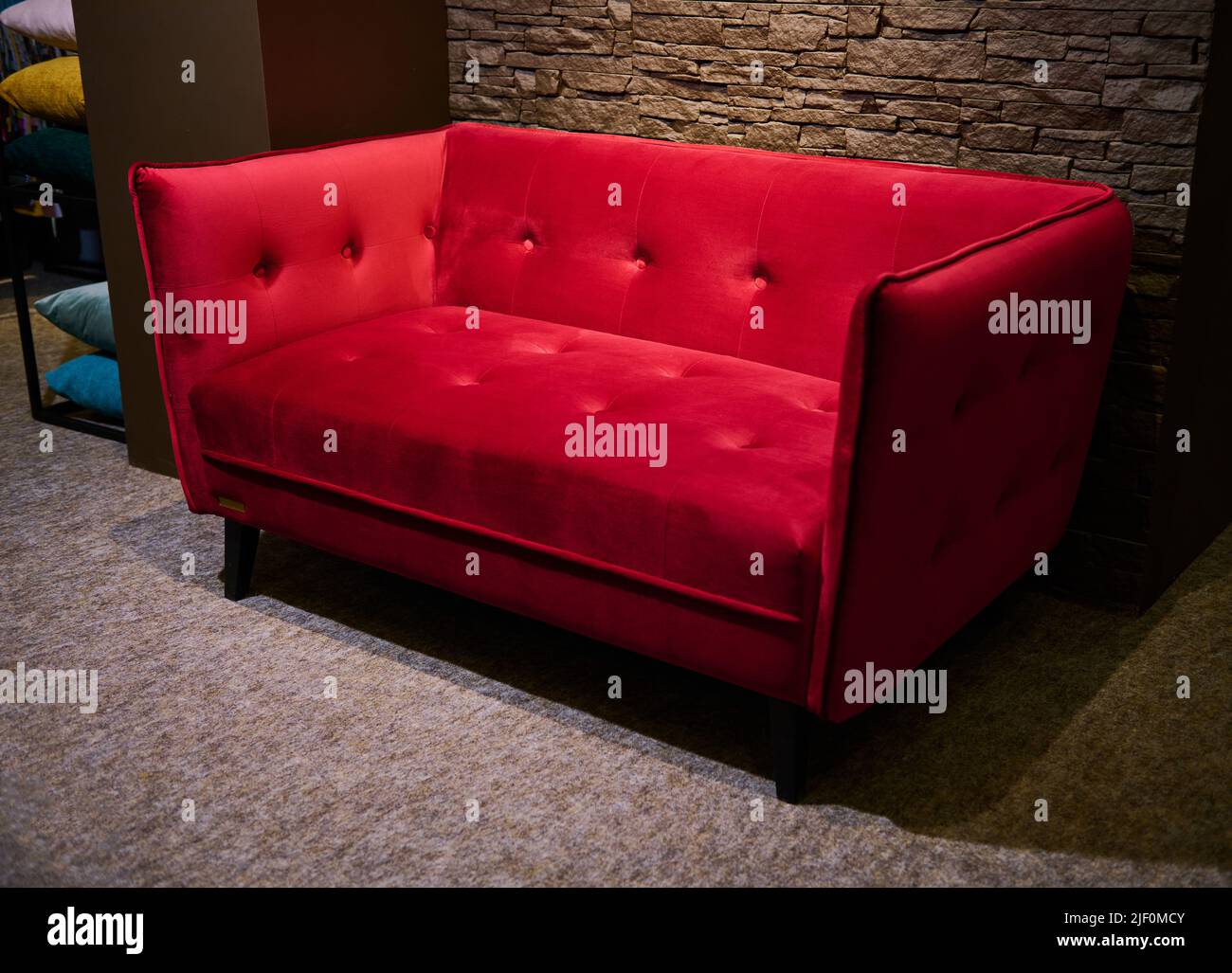 Stilvolles Jugendstil-Polstersofa in leuchtendem Rot, das im Möbeldesign-Geschäft gegen die stilvolle Backsteinwand im Möbelraum zum Verkauf steht Stockfoto