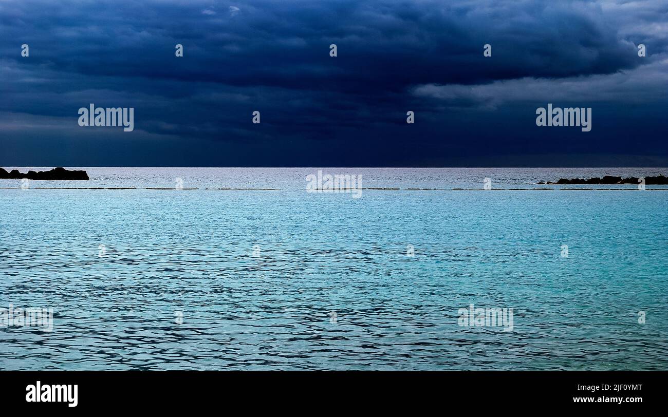 Leuchtendes blaues Meer und dunkelblaue Wolken am Himmel über dem Horizont Stockfoto