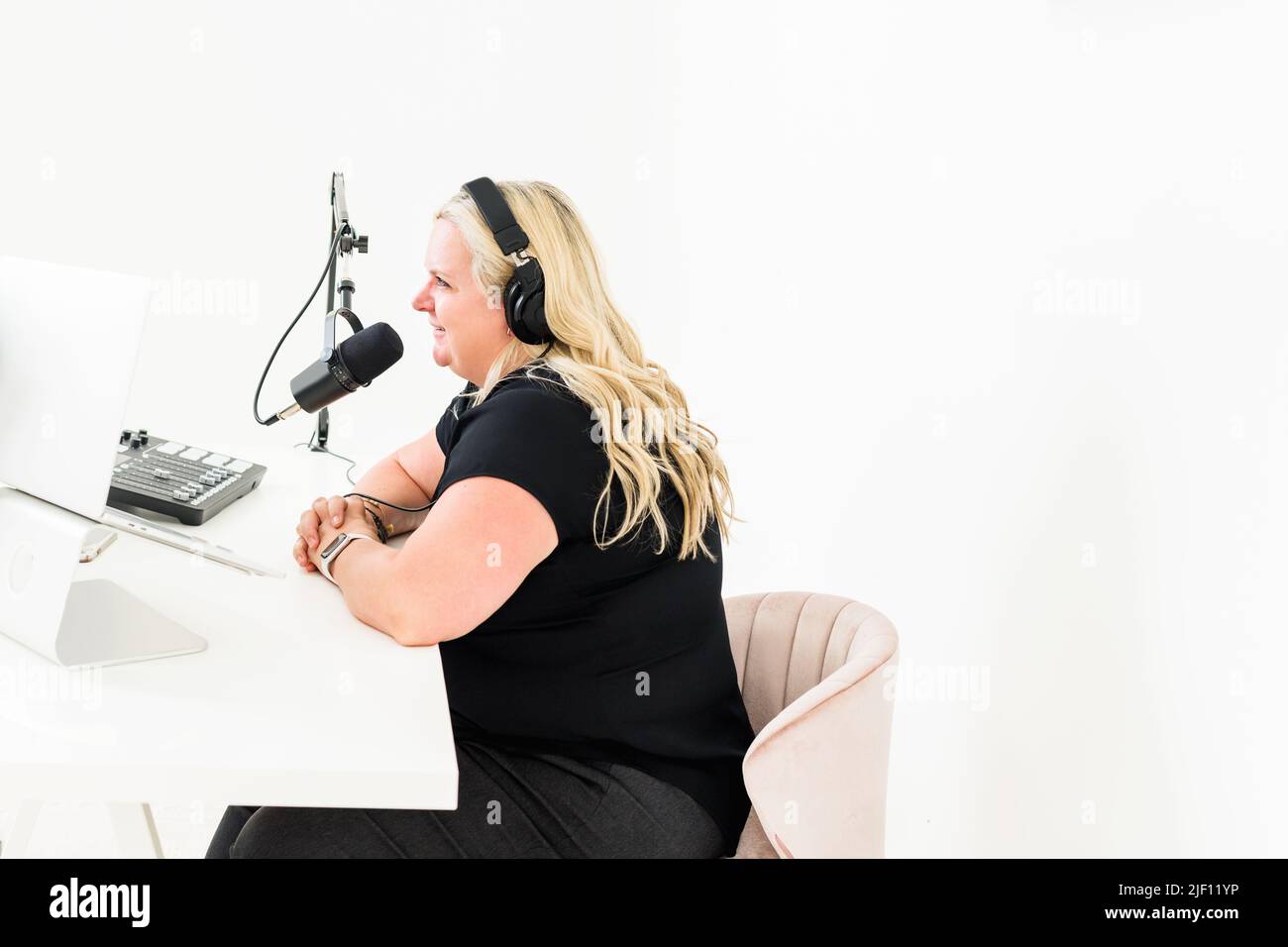 Frau mit Kopfhörern, die am Schreibtisch ins Mikrofon spricht Stockfoto
