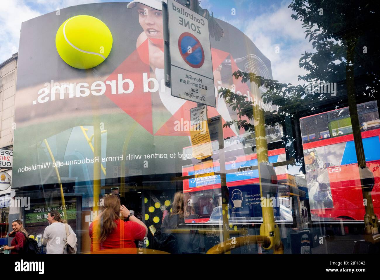 Im Fenster eines Busses spiegelt sich die britische Tennisspielerin Emma Raducanu am ersten Wettkampftag während der Wimbledon Lawn Tennis Association Championships am 27.. Juni 2022 in London, England, auf einer riesigen Werbetafel im Stadtzentrum von Wimbledon wider. Stockfoto