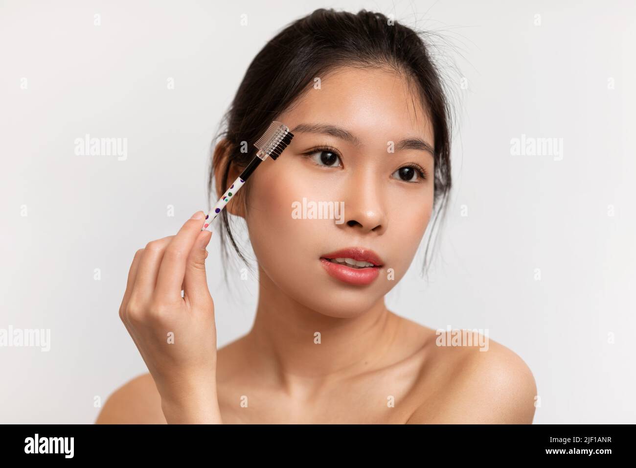 Natürliches Make-up-Konzept. Junge koreanische Dame putzt die Augenbrauen, hält die Bürste und macht morgendliche Schönheitsroutine Stockfoto