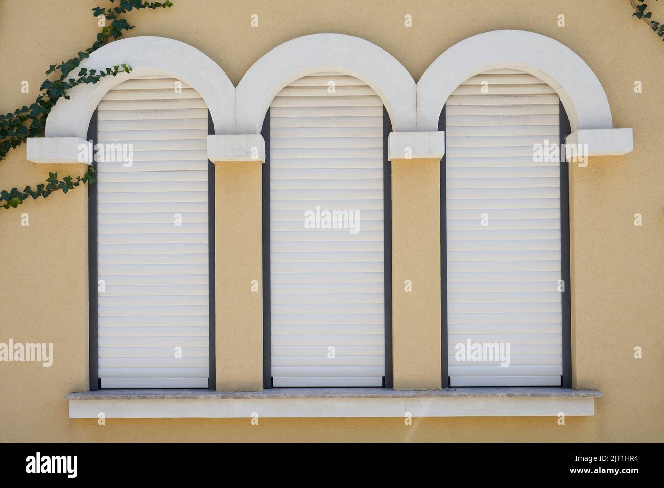 Weiße Rollläden an schmalen Fenstern in einem Gebäude. Stockfoto
