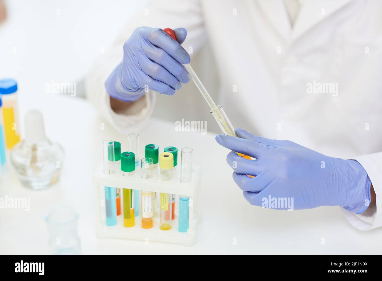 Nahaufnahme eines nicht erkennbaren Wissenschaftlers in Gummihandschuhen, die am Schreibtisch mit Reagenzglasgestell sitzen und die Probe für Labortests vorbereiten Stockfoto