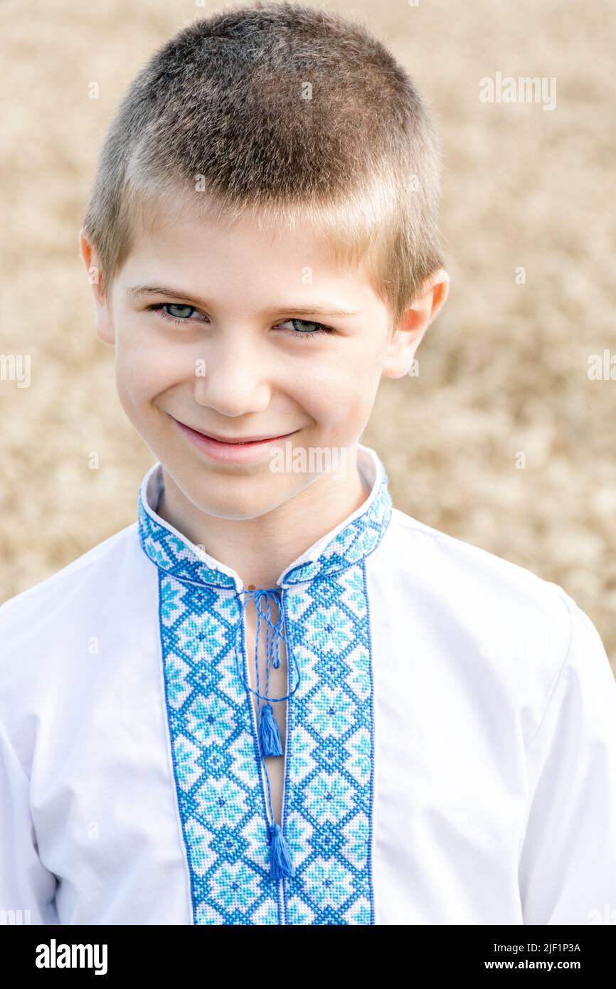 Porträt eines Schuljungen in einem traditionellen, bestickten ukrainischen Hemd auf dem Hintergrund des Weizenfeldes am sonnigen Tag. Blaue Stickerei. Kind lächelt aufrichtig. Unabhängigkeitstag, Verfassung der Ukraine. Stockfoto