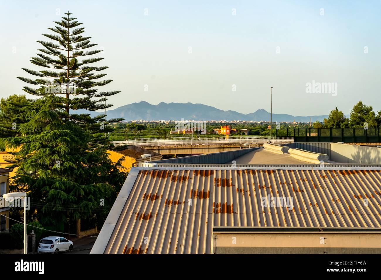 Blick auf eine Stadtlandschaft mit einer Straße, einem großen Baum und den Bergen im Hintergrund. Stockfoto