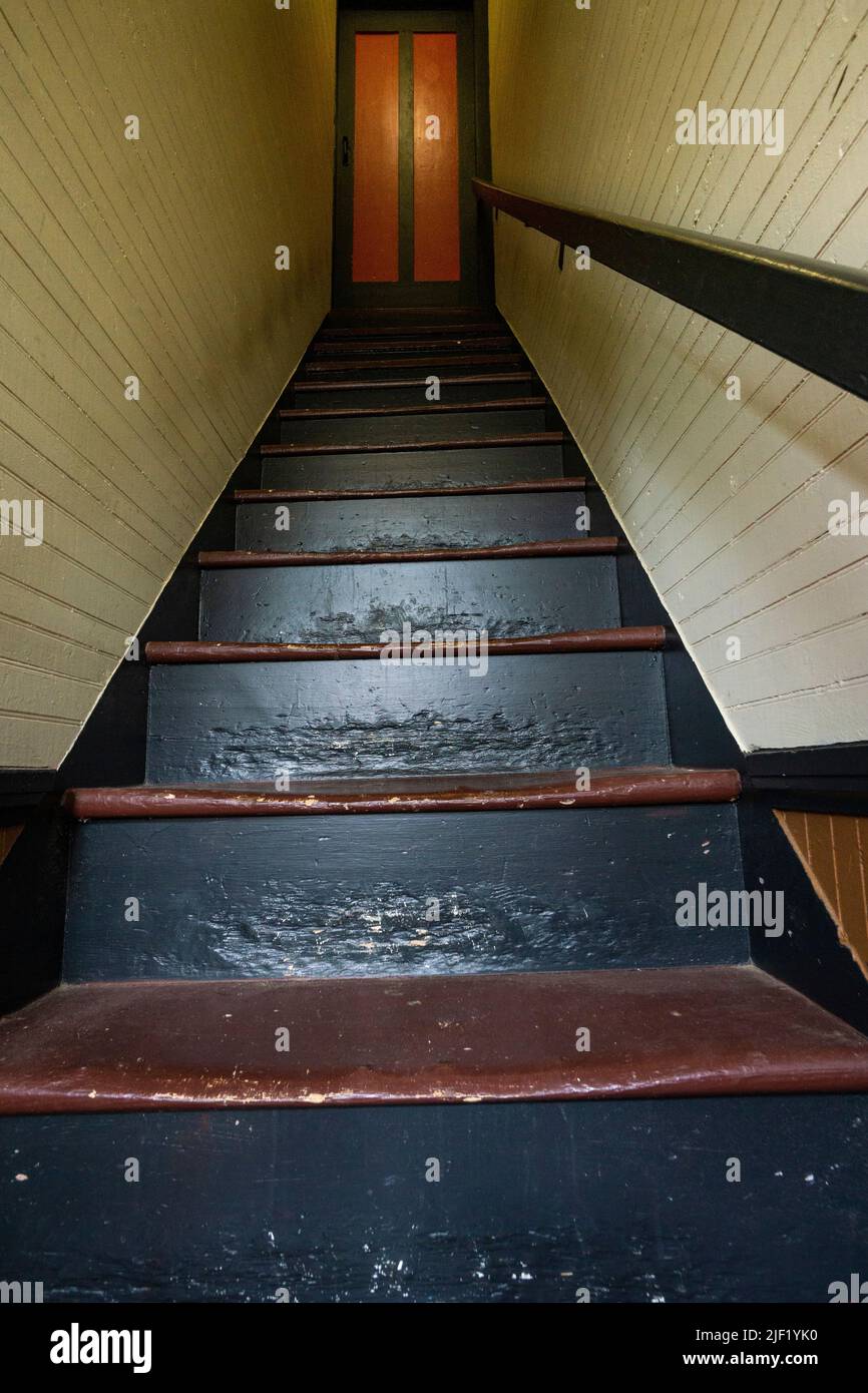 Steile und schmale Holztreppe mit einem Eingang oben. Stockfoto