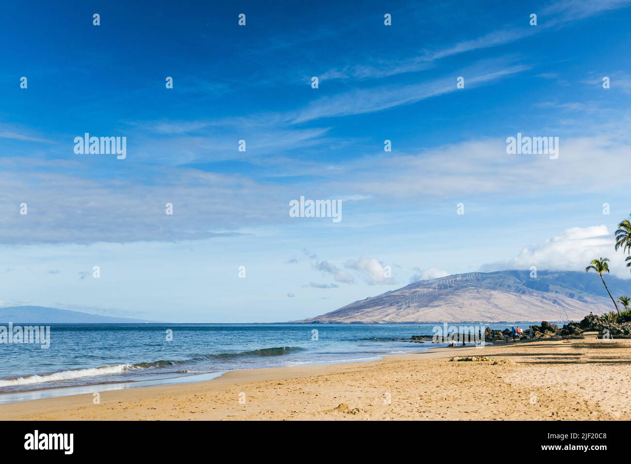 Ein Strand auf Maui Hawaii mit Sand, Wellen und einem Berg in der Ferne. Stockfoto