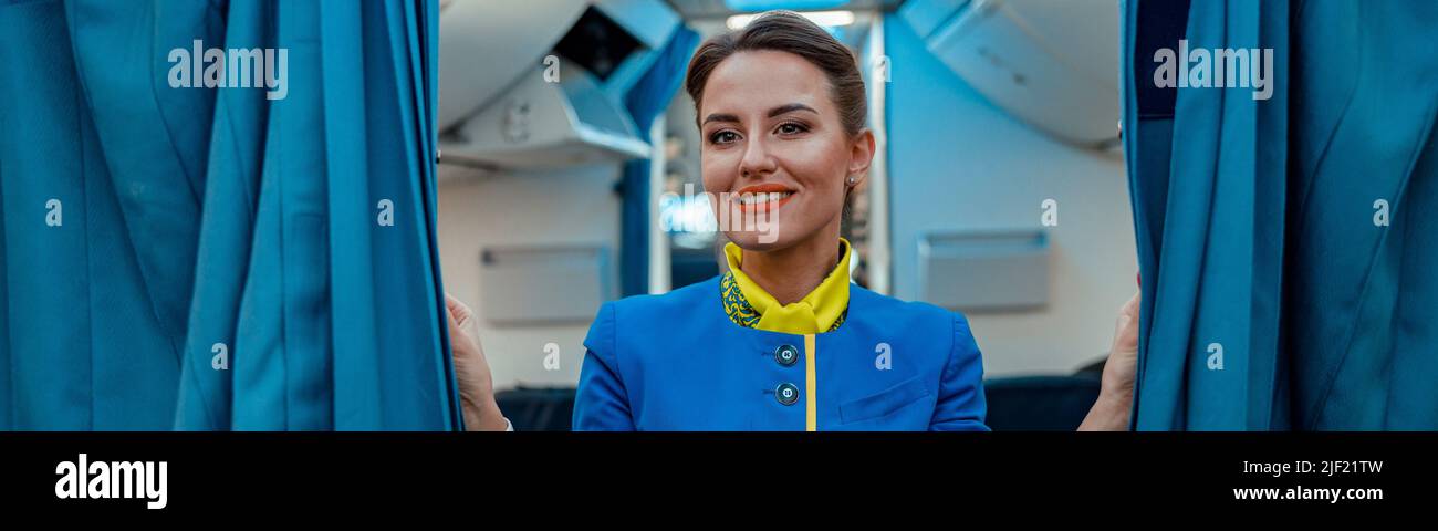 Fröhliche Frau Stewardess hält Vorhänge in Passagierflugzeugen Stockfoto