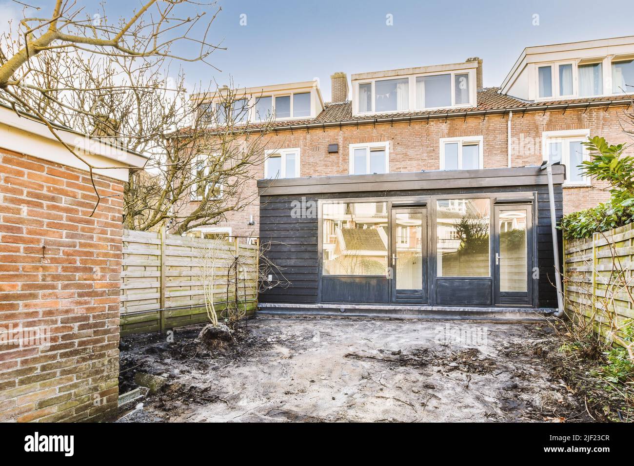 Unordentlicher Innenhof mit Holzzaun, Mülltonnen und Lehmziegelhaus Stockfoto