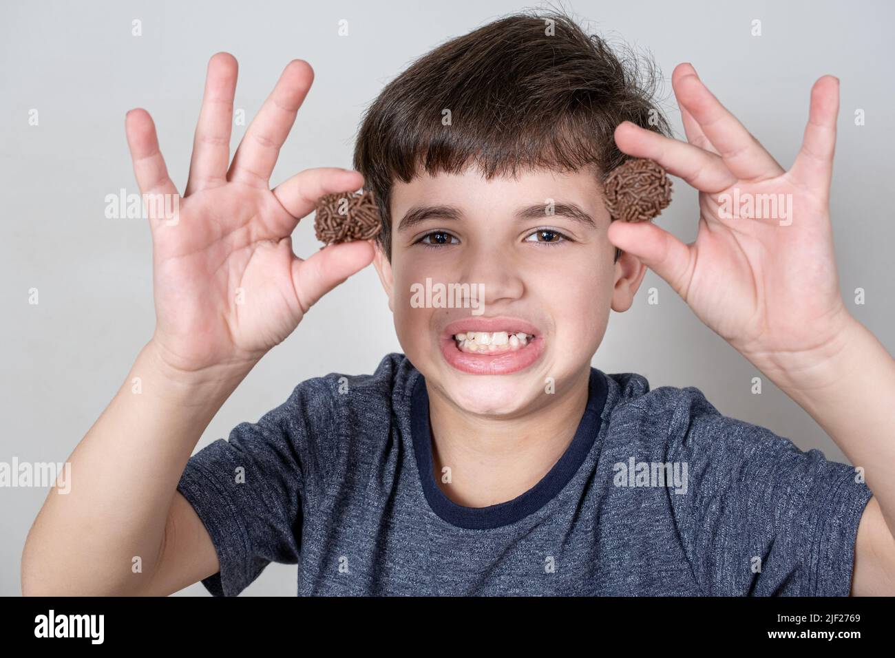 Der 9-jährige Brasilianer entblößt seine Zähne und hält zwei brasilianische Fudge-Kugeln. Stockfoto