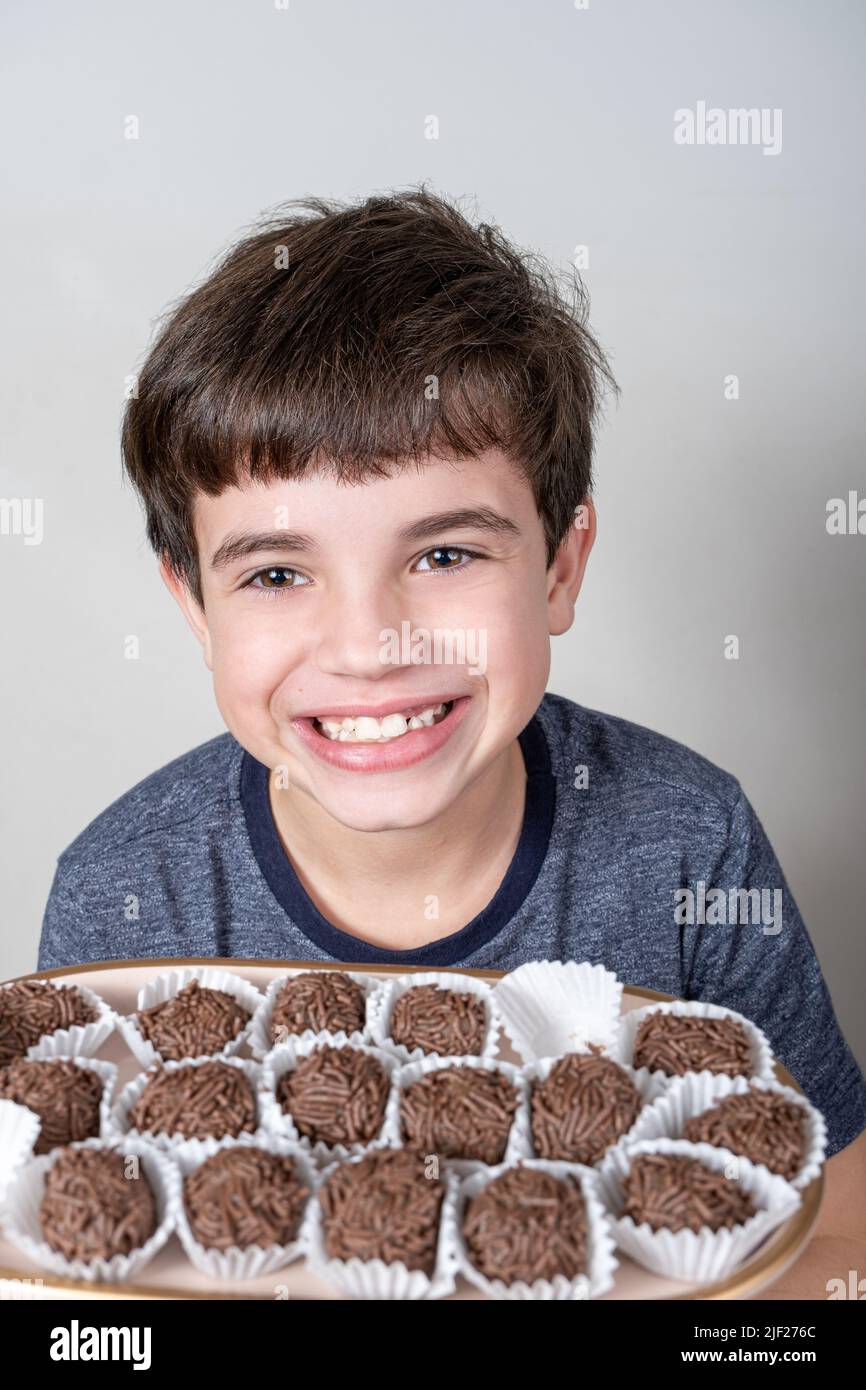 9-jähriges Kind, das ein Tablett mit mehreren brasilianischen Fudge-Bällen und einem großen Lächeln in der Hand hält. Stockfoto