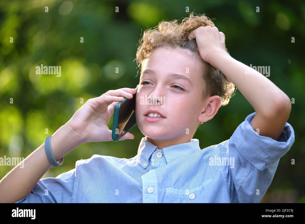 Junger, rätselhafter Junge, der im Sommerpark mit dem Handy telefoniert Stockfoto