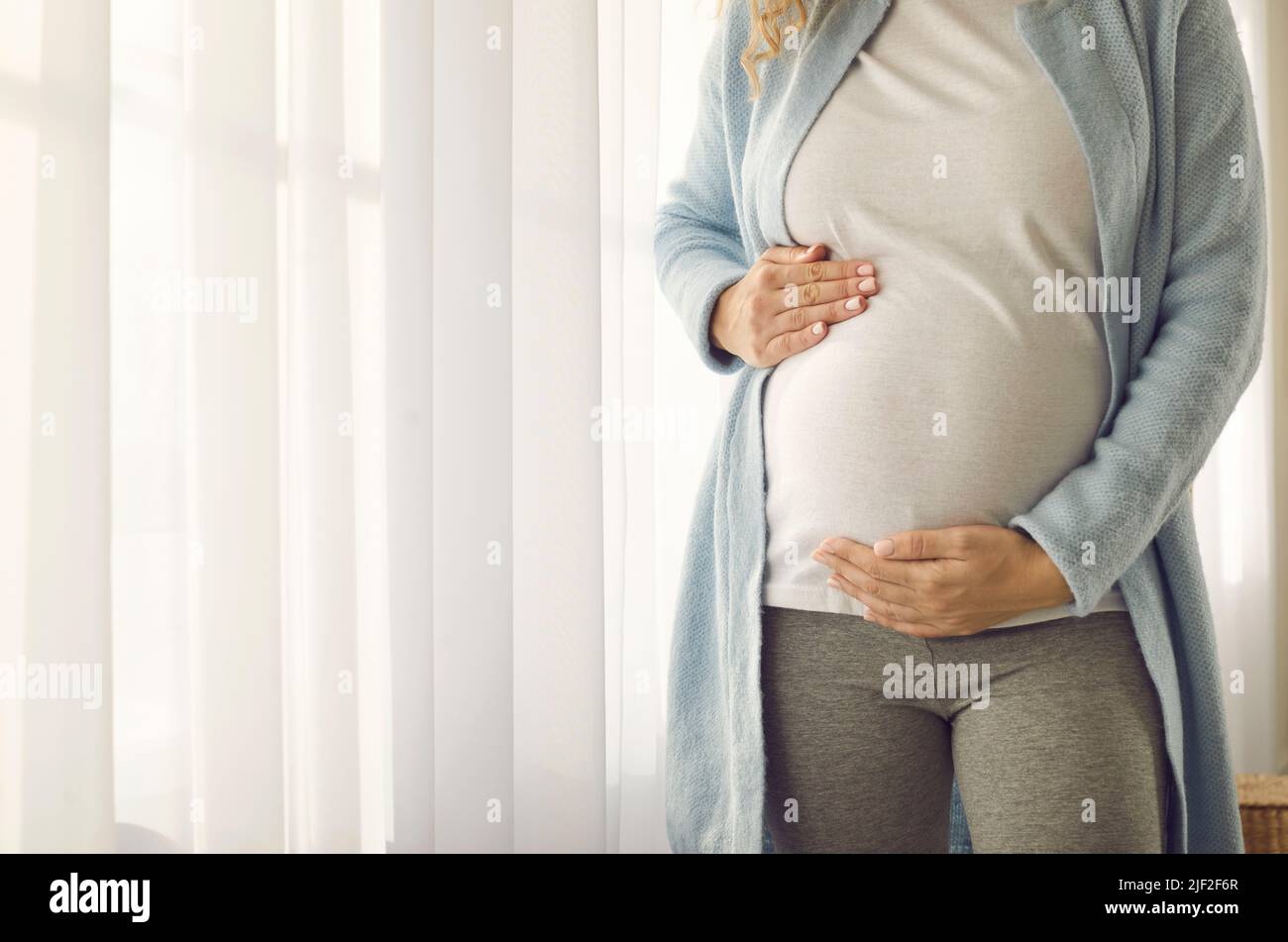 Bauch einer Schwangeren, die ihn sanft mit ihren Händen unterstützt, um das Baby zu treffen. Stockfoto