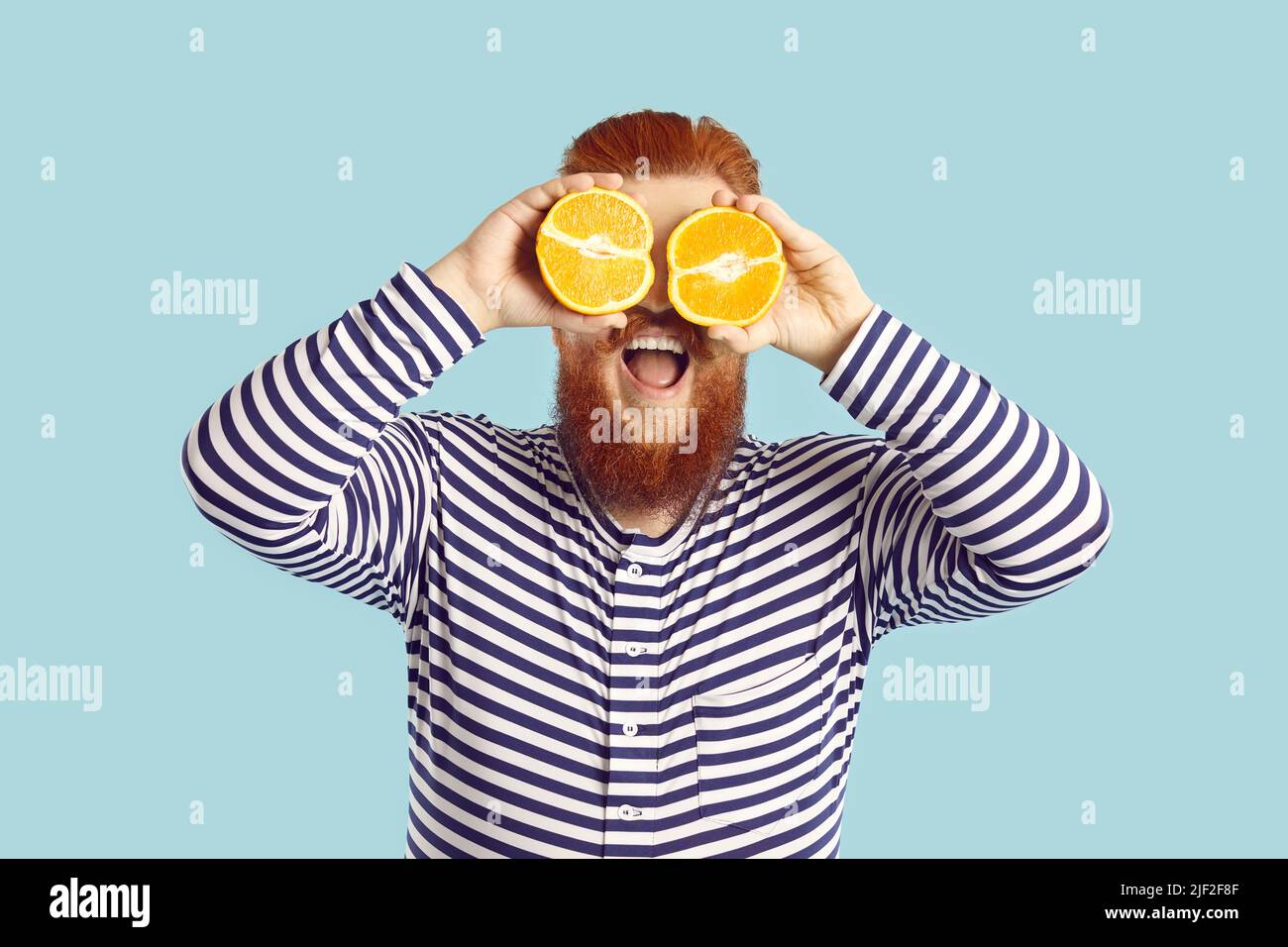 Lustiger Mann hält Hälften von saftigen Zitrusfrüchten und schließt seine Augen auf hellblauem Hintergrund. Stockfoto