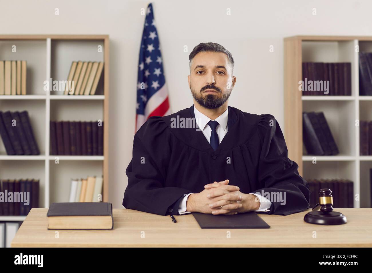 Junger Richter in einem Kleid, der mit einem Gavel in einem amerikanischen Gerichtsgebäude an seinem Tisch sitzt Stockfoto