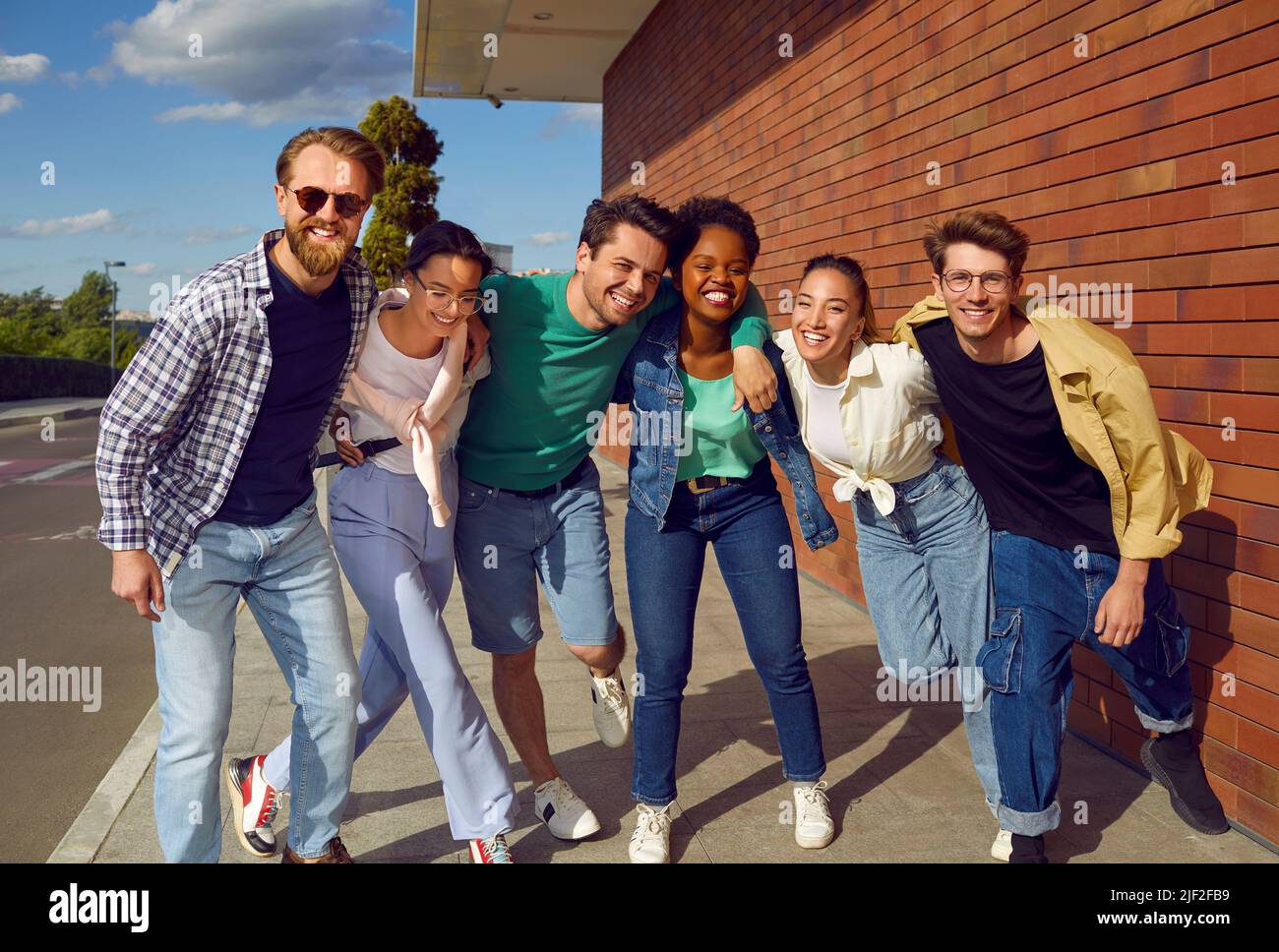 Unbeschwerte internationale Gruppe von Freunden in lässigen Outfits lächeln und umarmen auf der Straße. Stockfoto