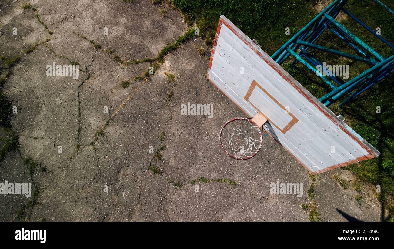 Altes Basketball-Backboard. Aus Brettern. Abblätternde Farbe und ein beschädigter Korb. Auf dem Gelände befindet sich ein alter gesprungener Asphalt. Von oben aufgenommen. Antenne Stockfoto