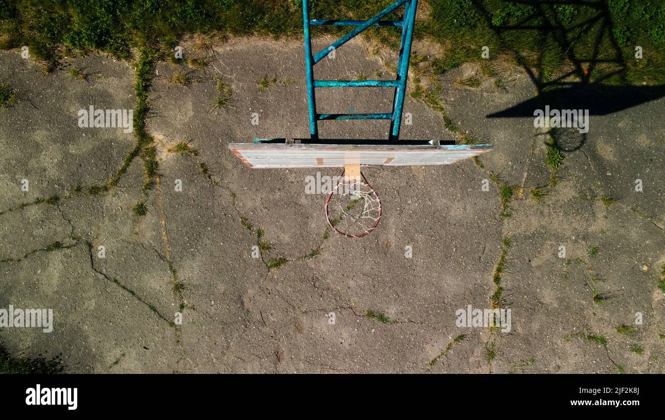 Altes Basketball-Backboard. Aus Brettern. Abblätternde Farbe und ein beschädigter Korb. Auf dem Gelände befindet sich ein alter gesprungener Asphalt. Von oben aufgenommen. Antenne Stockfoto