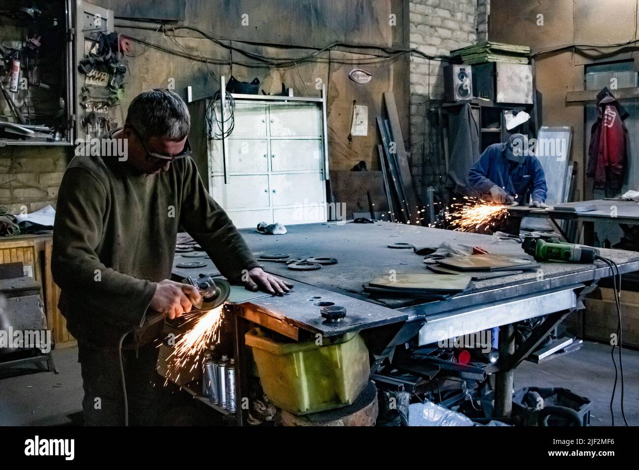 Zwei ukrainische Männer Formen Metallplatten mit einem Winkelschleifer. Ukrainische Zivilisten haben ihren Werkstattraum in eine kleine Fabrik in Zaporizhzhya verwandelt, wo die Front nur etwa 50 Kilometer von der Stadt entfernt ist. Sie produzieren handgefertigte kugelsichere Platten als Körperpanzerung für das ukrainische Militär und Zivilisten, die gegen die Invasion in Russiaís kämpfen. Sie arbeiten Tag für Tag aufgrund der großen Nachfrage. Stockfoto