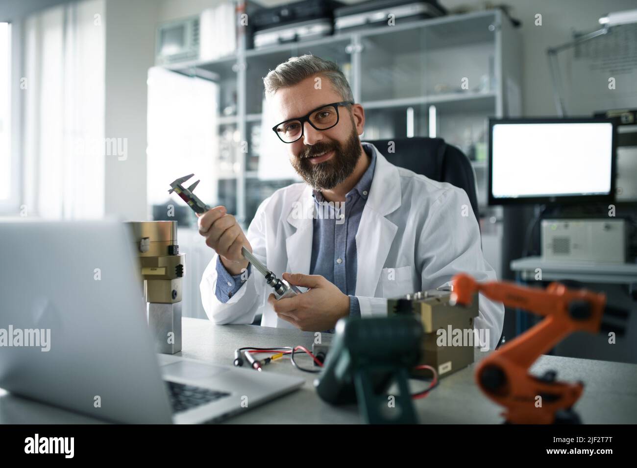 Roboteringenieur, der am Design eines modernen Roboterarms arbeitet und im Labor am Schreibtisch sitzt. Stockfoto