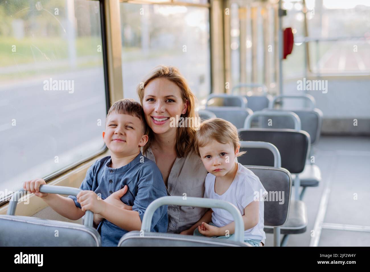 Junge Mutter mit kleinen Kindern, die im Sommer in der Straßenbahn unterwegs sind, pendeln und ein nachhaltiges Lifestyle-Konzept entwickeln. Stockfoto