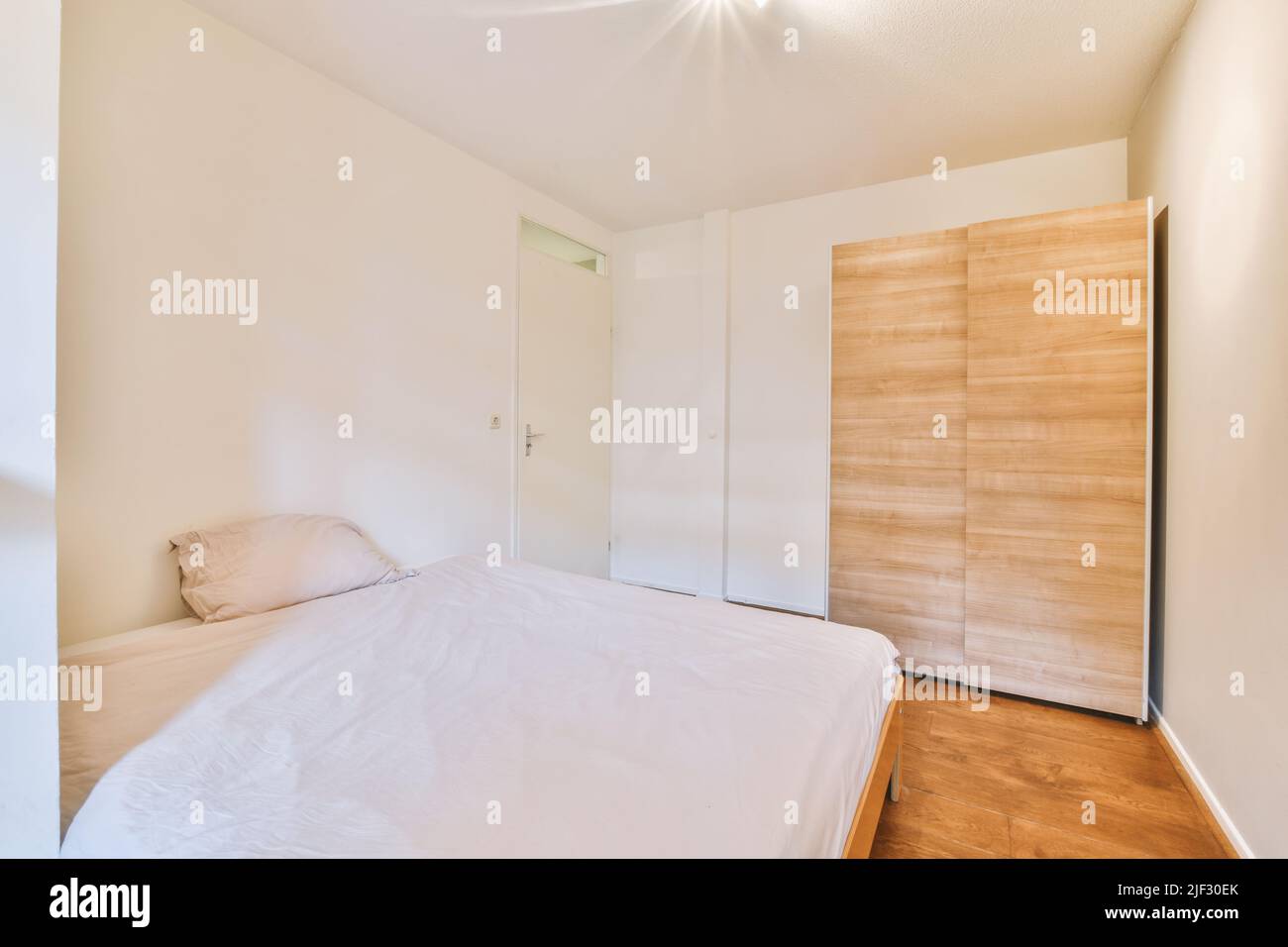 Komfortables Bett mit dekorativer Decke in der Nähe der Glastür und des Kleiderschrankes im hellen Schlafzimmer Stockfoto