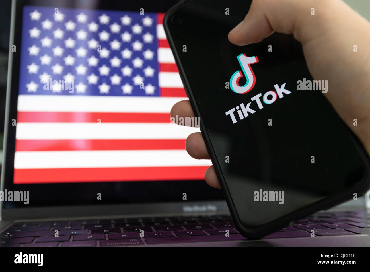 TikTok-App auf dem Smartphone und Flagge der Vereinigten Staaten von Amerika im Hintergrund. Stockfoto